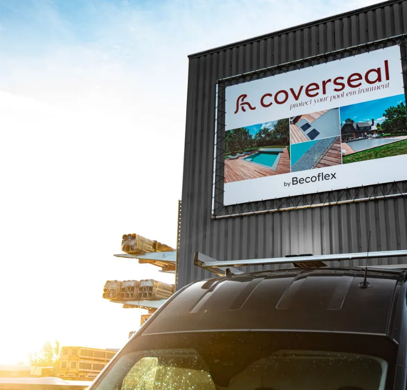 notre-entreprise Affiche "Coverseal" sur un bâtiment gris, avec des images de piscines, un ciel bleu et une voiture noire au premier plan.