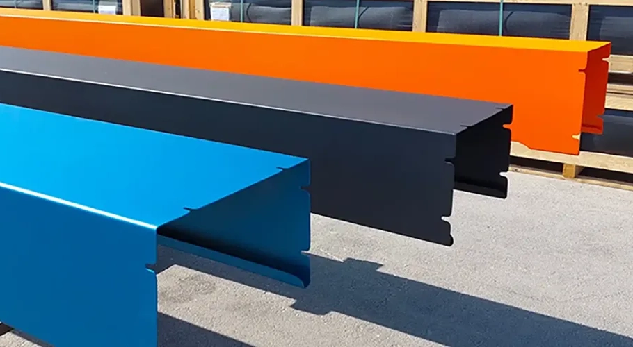 barres-metalliques-bleues-noires-orange Trois profilés métalliques colorés, en bleu, noir et orange, sont alignés horizontalement sur une surface grise.
