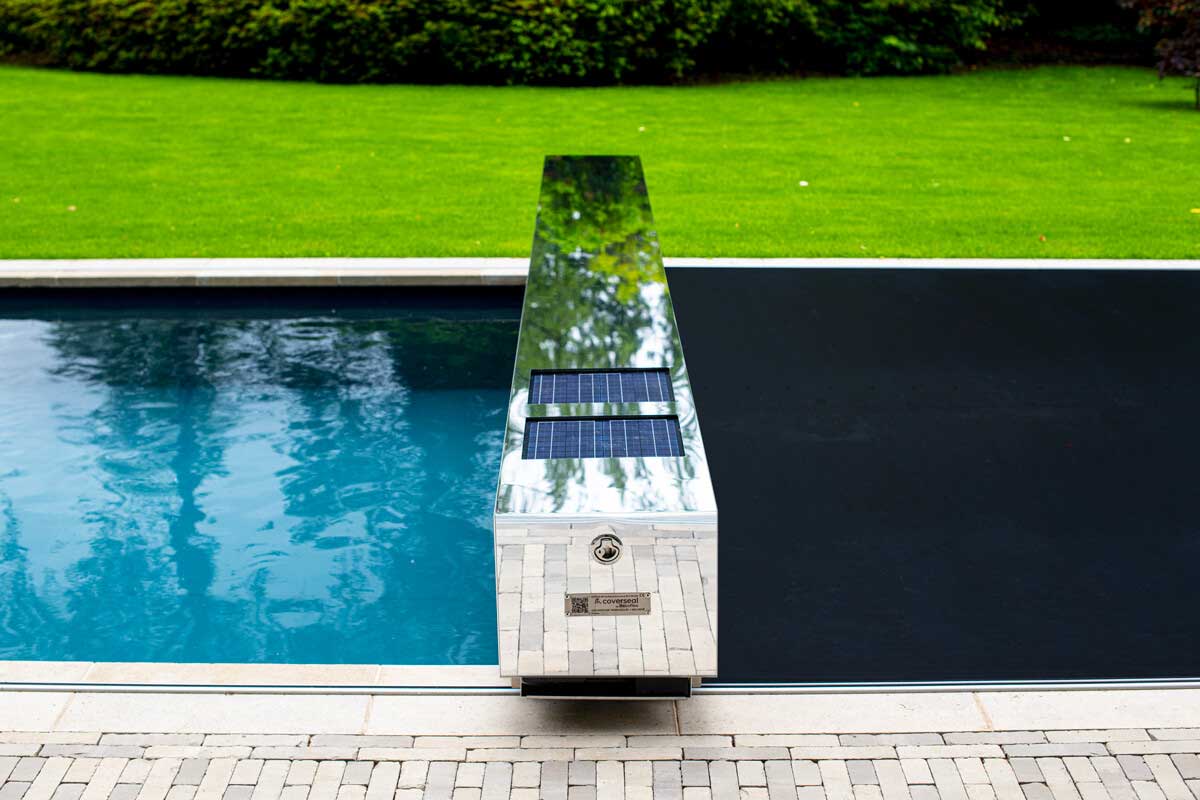 Coverseal-Effet-Miroir Une couverture de piscine avec un effet miroir et des panneaux solaires, entourée d'une pelouse verte et d'un carrelage beige.
