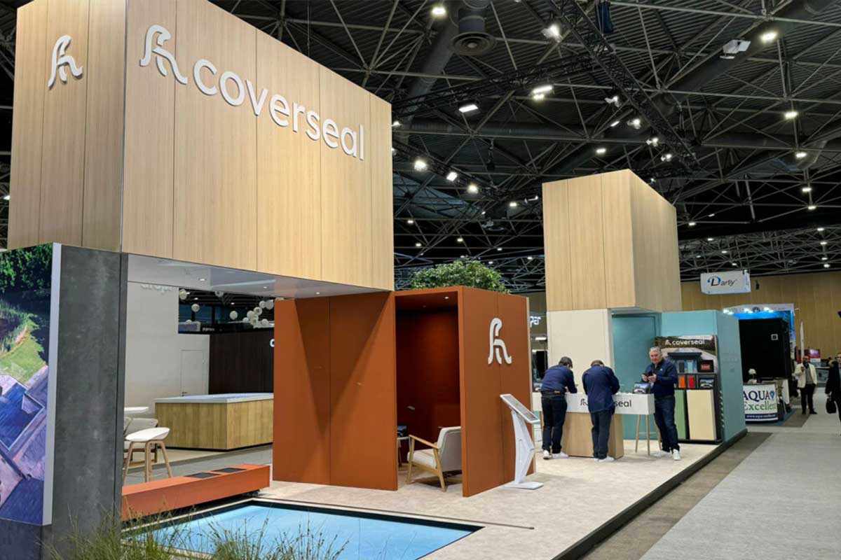 Stand Coverseal Stand d'exposition Coverseal avec structures en bois clair et panneaux orange, deux personnes interagissent près d'un comptoir.