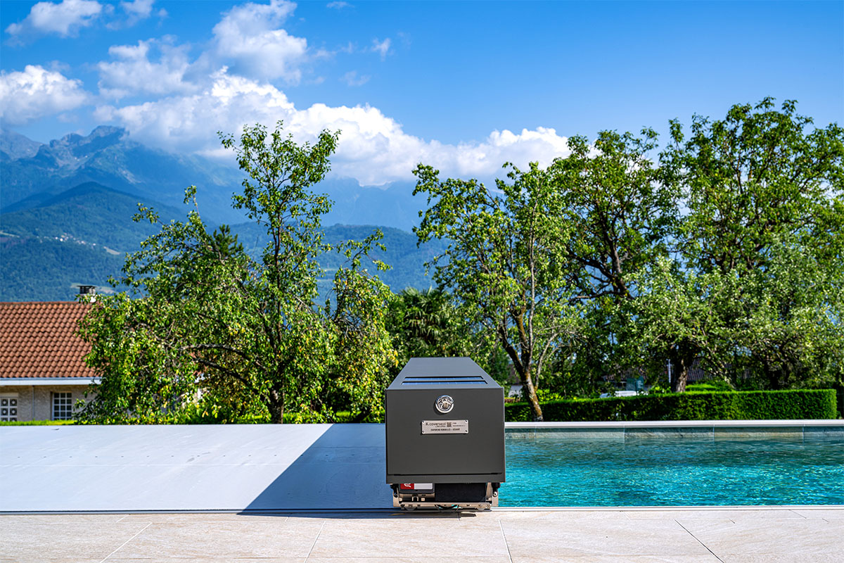 La-grange-des-alpes1 Couverture Coverseal fermée sur une piscine, avec boîtier de mécanisme gris et vue panoramique sur les montagnes et la verdure environnante.