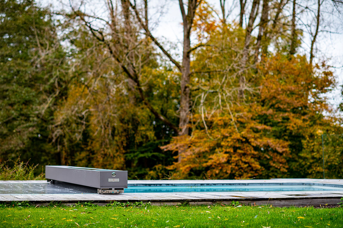 Pond3 Piscine design équipée d’une couverture Coverseal, intégrée dans une terrasse en bois au cœur d’un grand jardin arboré.