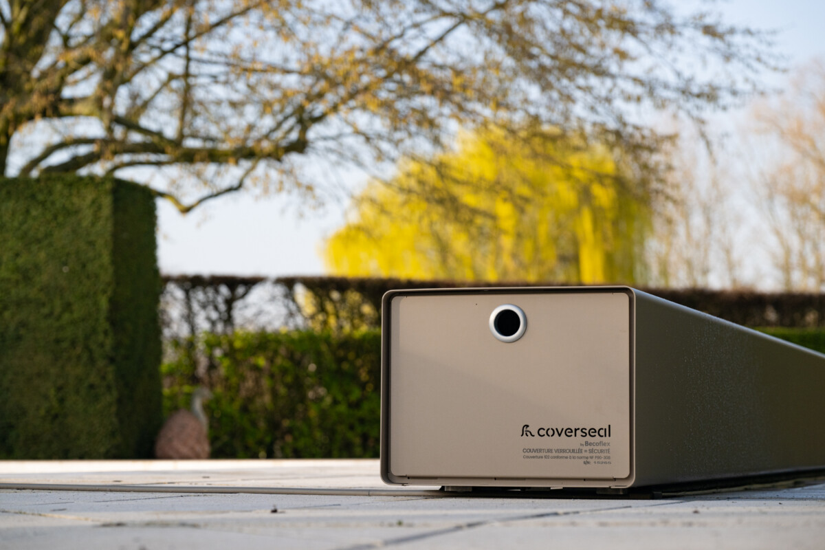 Couverture Coverseal fermée sur une piscine, avec boîtier de mécanisme gris et vue panoramique sur les montagnes et la verdure environnante.