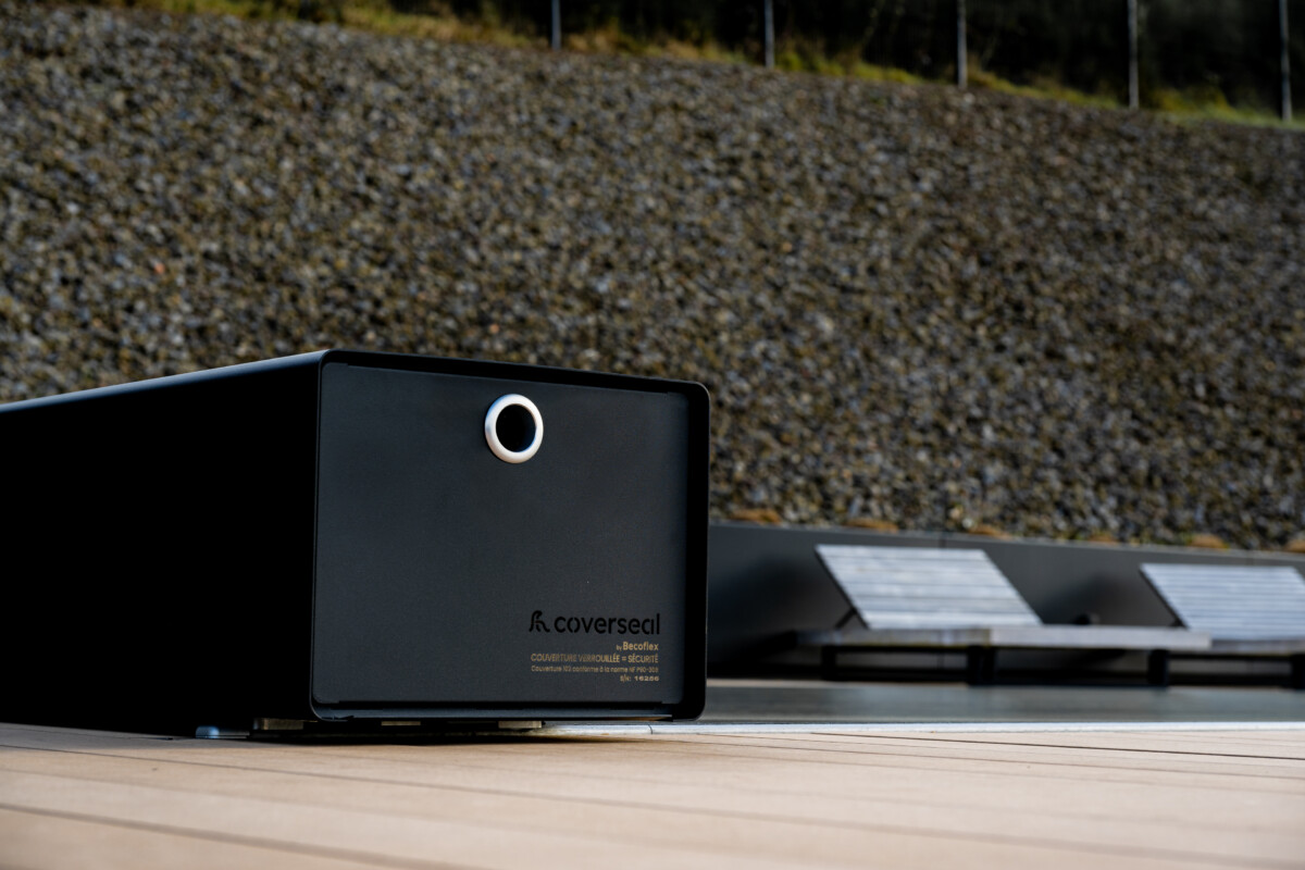 Couverture Coverseal fermée sur une piscine, avec boîtier de mécanisme gris et vue panoramique sur les montagnes et la verdure environnante.