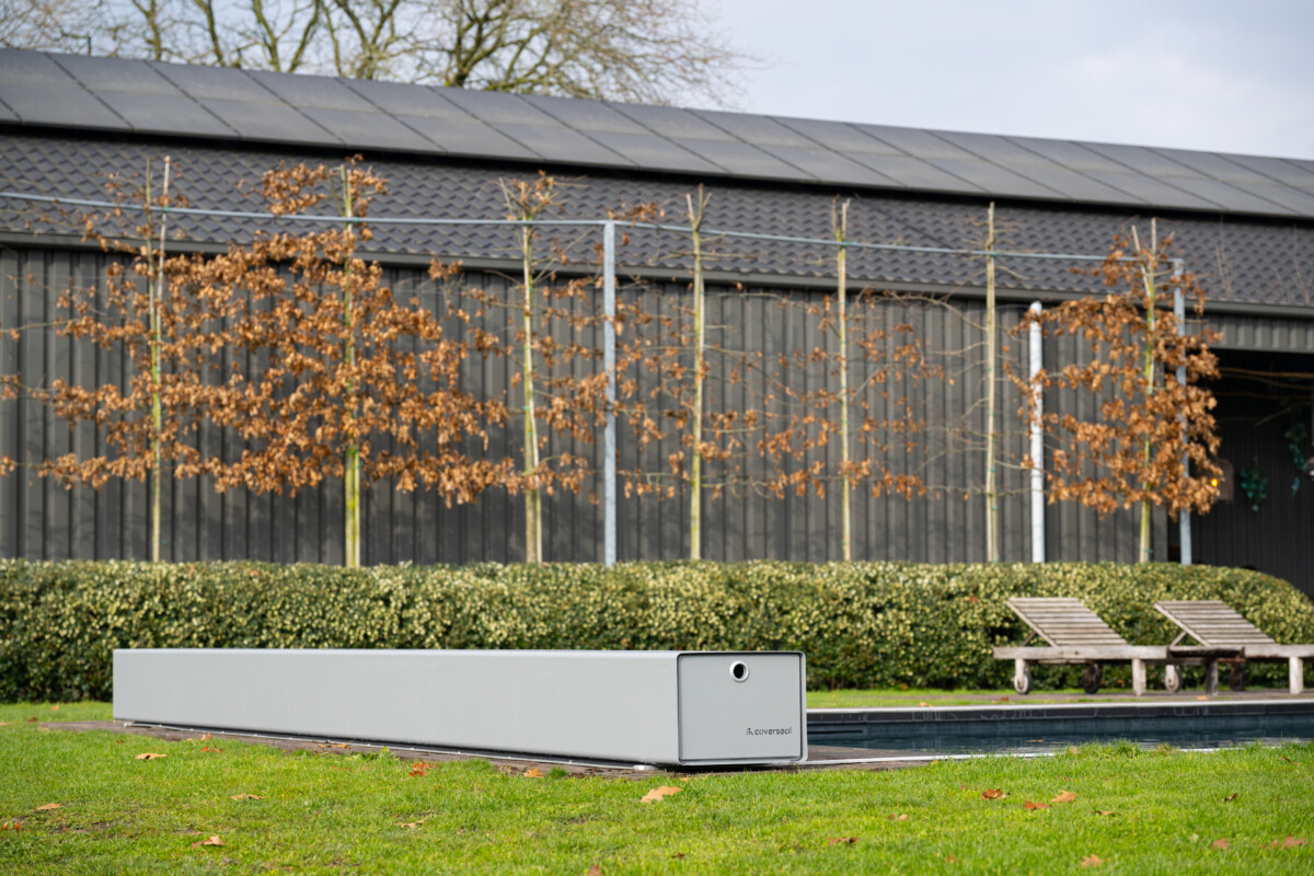 Couverture Coverseal fermée sur une piscine, avec boîtier de mécanisme gris et vue panoramique sur les montagnes et la verdure environnante.