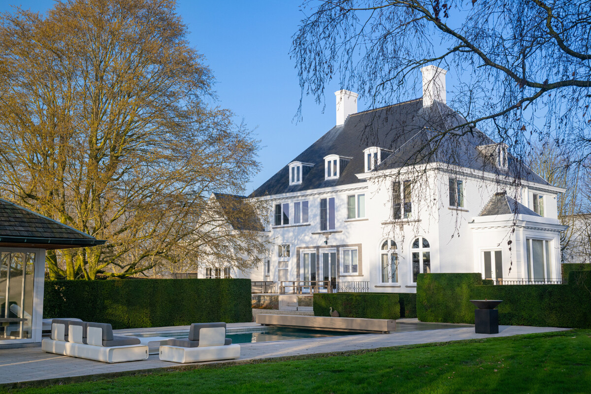 Maison en pierre de style chalet alpin avec grande baie vitrée donnant sur une terrasse et une piscine protégée par une couverture Coverseal.